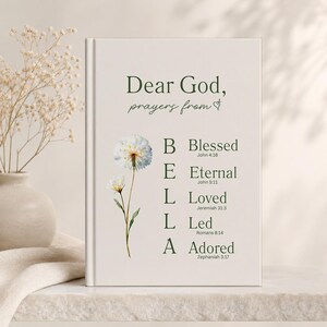 May include: A hardcover journal with the text "Dear God, prayers from" and the word "BELLA" spelled out vertically. Each letter corresponds to a word: Blessed, Eternal, Loved, Led, and Adored, with Bible verses. A watercolor dandelion is on the left.