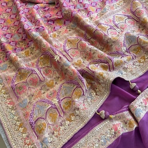 May include: A purple fabric garment featuring a complex pattern of small hexagonal shapes containing animal motifs in shades of pink, orange, and gold. The border is embellished with metallic embroidery, sequins, and dangling purple tassels.