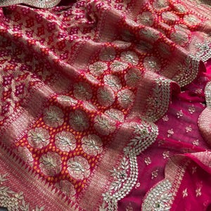 May include: A vibrant fuchsia and red textile featuring intricate gold metallic embroidery in circular floral patterns. The fabric displays a traditional tie-dye effect with small yellow dots and a scalloped border embellished with gold thread.