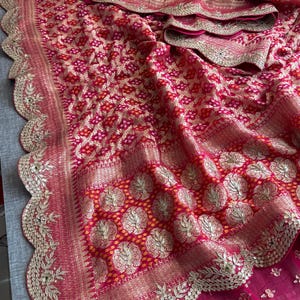 May include: A vibrant fuchsia and red fabric featuring a dense, intricate pattern of small white dots and gold metallic floral motifs. The textile is finished with a wide, scalloped border embellished with detailed gold embroidery and sequins.