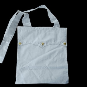 Könnte beinhalten: Eine hellblaue Tragetasche mit einer Klappentasche, die mit zwei goldfarbenen Metallknöpfen befestigt ist. Die Tasche hat einen langen Riemen zum Über-der-Schulter-Tragen. Die Tasche ist aus einem weichen, hellfarbigen Stoff gefertigt.