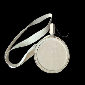 Puede incluir: Una cantimplora redonda de madera clara con un tapón de madera a juego y una correa de lona blanca. La cantimplora tiene un diseño circular con un patrón de veta de madera clara y una estética sencilla y clásica.