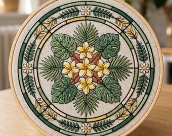 May include: A circular embroidery hoop containing a piece of beige fabric with a hand-stitched design. The pattern features a central cluster of yellow plumeria flowers surrounded by green monstera and palm leaves, enclosed in a decorative border.