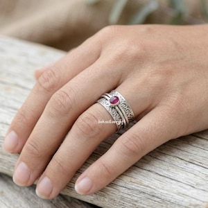 May include: A silver ring with a red gemstone is worn on a finger. The ring has an ornate, swirling design and the text "bohosilvergift". The gemstone is oval-shaped and set in a silver band.