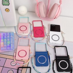 May include: A collection of phone cases in various colors, including pink, red, blue, and black, each with a circular design. A pink cat ear headset sits on a stand. A keyboard and stickers are also visible.