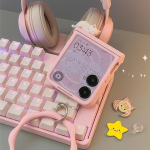 Può includere: Un'impostazione di gioco rosa con tastiera, cuffie con orecchie da gatto e un telefono che mostra un design a cartoni animati e l'ora 03:43. Gli accessori includono un cinturino da polso rosa e spille decorative.