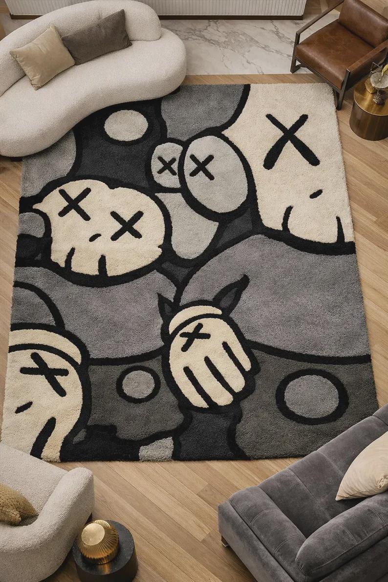May include: A rectangular area rug featuring a graphic pattern of stylized cartoon characters in shades of gray, black, and cream. The design includes multiple faces with X-shaped eyes and gloved hands with X symbols, rendered in a thick, textured pile.