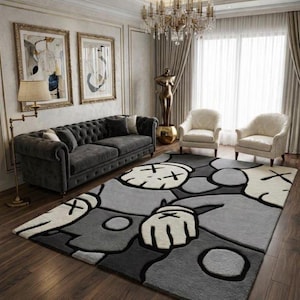 May include: A modern living room featuring a gray tufted sofa, two white armchairs, and a patterned rug with cartoon-like figures in shades of gray, black, and white. The room is decorated with artwork, a floor lamp, and a chandelier.