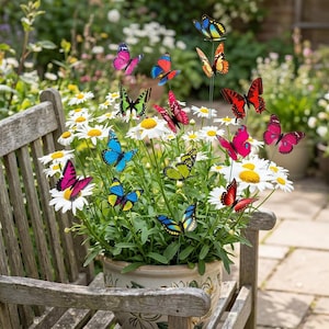 Peut inclure: Un pot de marguerites blanches orné de décorations de papillons colorés. Les papillons sont de différentes couleurs, notamment rose, bleu, jaune et rouge. Le pot est posé sur un banc en bois dans un jardin.