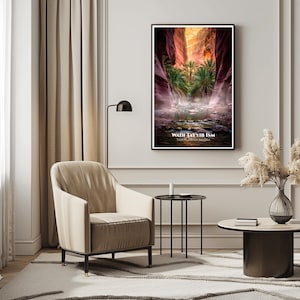 May include: A framed art print featuring a scenic view of a canyon with palm trees and a stream. The image has a black frame and the text "WADI TAYYIB ISM TABUK SAUDI ARABIA" at the bottom. The artwork is displayed in a modern living room setting.