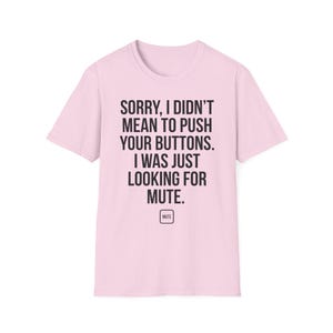 Może przedstawiać: Jasnoróżowa koszulka z czarnym napisem: "SORRY, I DIDN'T MEAN TO PUSH YOUR BUTTONS. I WAS JUST LOOKING FOR MUTE." Poniżej znajduje się mały kwadrat z napisem "MUTE".
