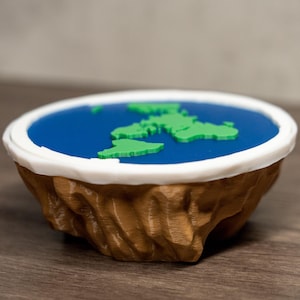 May include: A flat Earth model, featuring a blue ocean, green continents, and a brown, textured base with a white rim. The design is a humorous take on the globe, suitable for display.