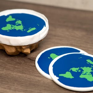 May include: A set of flat earth-themed coasters. The coasters have a blue ocean with green continents and a white border. One coaster is on a stand with a brown base, and two coasters are lying flat.