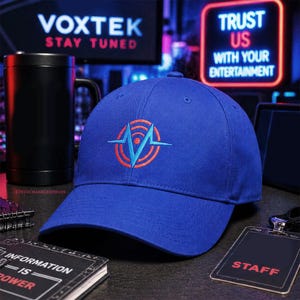 Peut inclure: Casquette de baseball bleue avec un logo brodé représentant un 'M' stylisé dans un cercle et un motif en forme de battement de cœur en rouge et bleu clair. La casquette est présentée avec un mug noir, un bloc-notes avec le texte "INFORMATION IS POWER" et un badge de personnel.