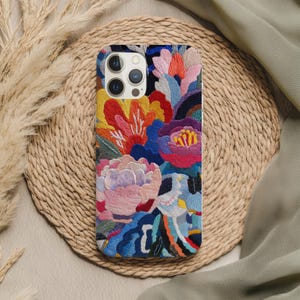 May include: A colorful phone case with an embroidered floral design. The case features a vibrant array of flowers in shades of pink, red, yellow, and blue. The intricate embroidery adds texture and detail to the phone accessory.