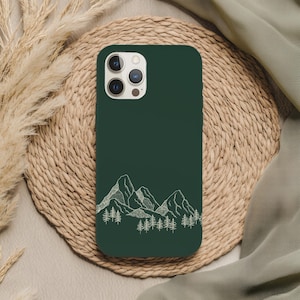 Könnte beinhalten: Dunkelgrüne Handyhülle mit einer weißen Strichzeichnung von Bergen und Kiefern. Die Hülle hat eine glatte Oberfläche und ist für ein Smartphone konzipiert. Das Design ist minimalistisch und naturbezogen.