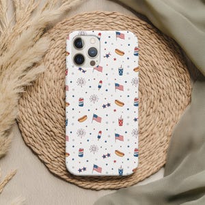 May include: A white phone case with a repeating pattern of American flags, hot dogs, soda cups, fireworks, and stars. The case has a glossy finish and is designed for a smartphone.