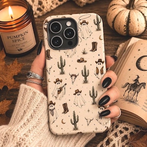 May include: A cream-colored phone case featuring a repeating pattern of ghosts wearing cowboy hats, cacti, cow skulls, and cowboy boots. The design includes small stars and crescent moons scattered across the surface in a brown ink illustration style.