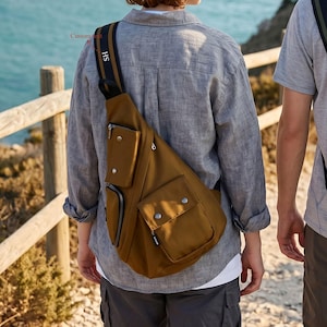 May include: A brown sling bag with multiple pockets and a black and white striped strap. The bag is worn over the shoulder and across the chest. The strap has the initials "SH" on it. The bag is made of a durable material and is suitable for outdoor activities.