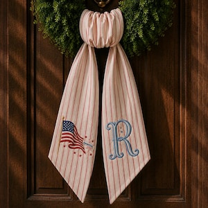 May include: Cream-colored door swag with red vertical stripes and a decorative bow. One side features an embroidered American flag and the text "America 2020". The other side has a blue embroidered letter "R".