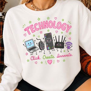 May include: A white crewneck sweatshirt featuring a colorful graphic with the text "TECHNOLOGY" and "Click. Create. Innovate." The design includes cartoon illustrations of a laptop, mouse, keyboard, router, and Wi-Fi symbol with faces.