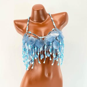 Könnte beinhalten: Ein Neckholder-Top aus durchscheinenden hellblauen runden Scheiben und einer Vielzahl kleiner Perlen in Weiß-, Hellblau- und Türkistönen. Das Design zeichnet sich durch mehrere herabhängende Perlenstränge aus, die einen Franseneffekt erzeugen.