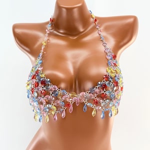 Könnte beinhalten: Ein farbenfrohes, mit Perlen besetztes Neckholder-Top mit roten, blauen, gelben und rosa Schmuckperlen. Das Top wird auf einer Schaufensterpuppe präsentiert und hat tropfenförmige Perlen am unteren Rand.