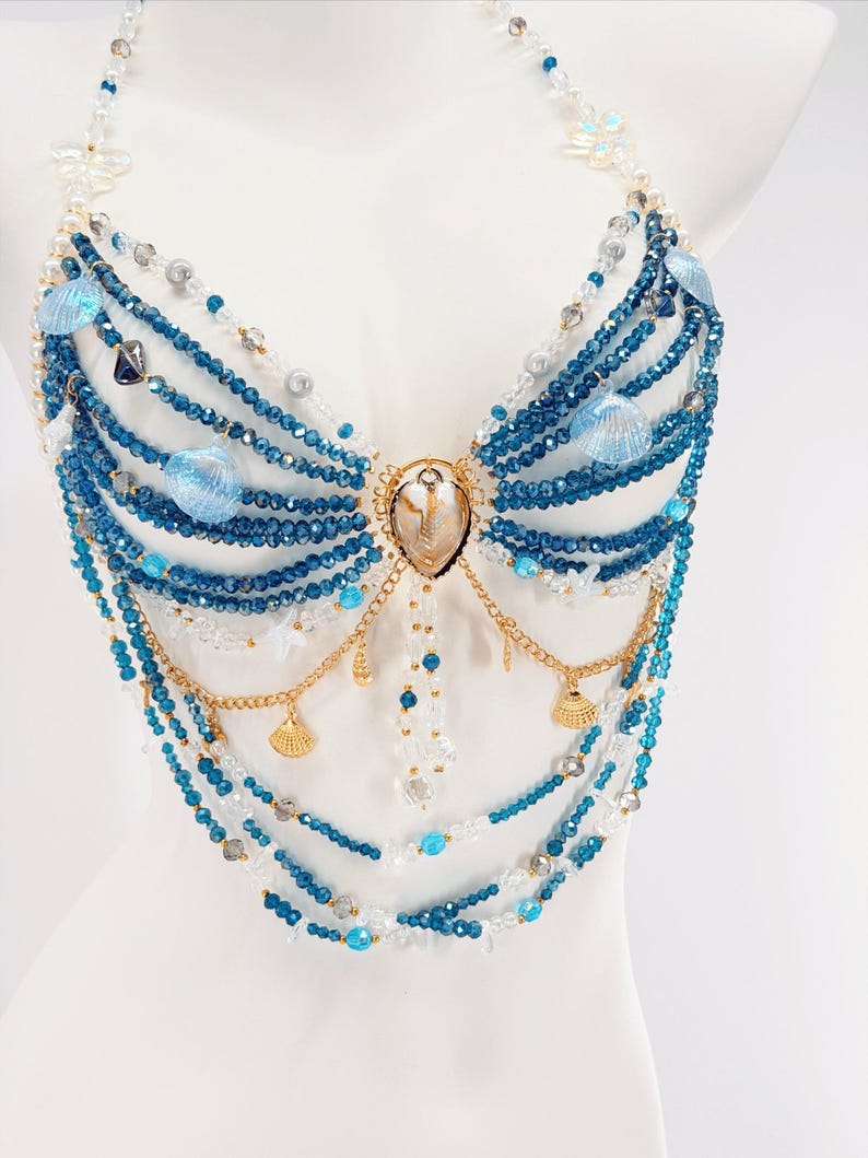 Pu&ograve; includere: Un top all'americana realizzato con molteplici fili di perline di cristallo blu e trasparenti. Il design presenta catene in metallo dorato, piccoli ciondoli a forma di conchiglia dorata e conchiglie blu iridescenti attorno a una conchiglia.