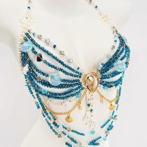 Pu&ograve; includere: Una catena per il corpo stile halter con molteplici fili di perline di cristallo blu profondo e trasparenti. Il design incorpora catene in metallo dorato, piccoli ciondoli a forma di conchiglia dorata e conchiglie blu iridescenti.