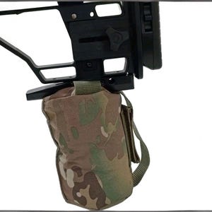 Può includere: Un calcio per fucile nero con una borsa con motivo mimetico attaccata. La borsa è nei toni del verde, marrone e beige. Il calcio ha un design complesso con più componenti e punti di regolazione.