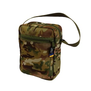 Peut inclure: Un sac bandoulière à motif camouflage avec une fermeture éclair et une sangle vertes. Le sac est de forme rectangulaire et comporte une petite étiquette aux couleurs bleu et jaune. Conçu pour transporter l'essentiel.