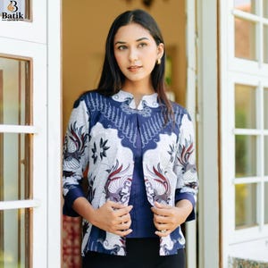 Puede incluir: Una camisa de manga larga con botones que presenta un patrón batik en azul marino y blanco con motivos de aves estilizadas. La prenda tiene un cuello mao, un panel central en azul marino sólido y mangas tres cuartos con puños sólidos.