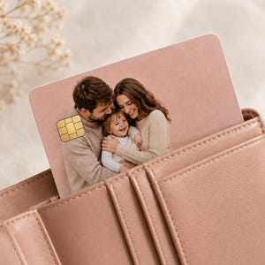 May include: A pink credit card with a family photo is partially inserted into a matching pink leather wallet. The card features a gold chip and a picture of a smiling family. The wallet has multiple card slots and a stitched design.