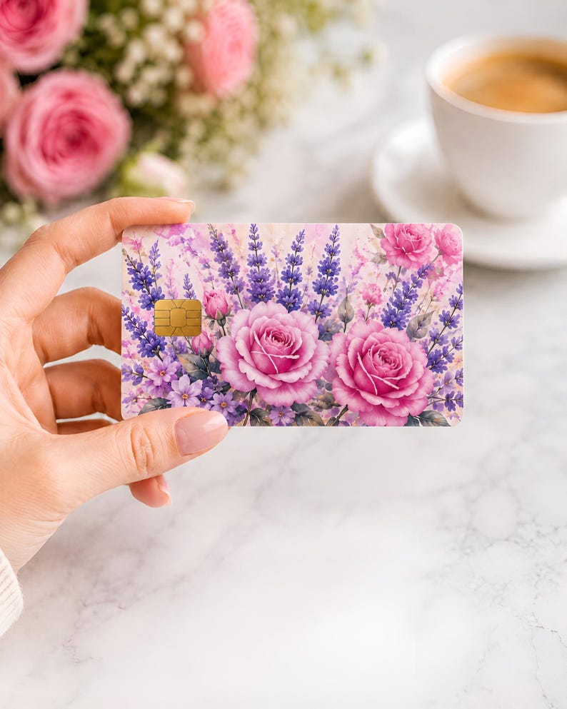 Puede incluir: Una tarjeta de cr&eacute;dito con dise&ntilde;o floral que presenta rosas rosas y lavanda p&uacute;rpura. La tarjeta tiene un chip dorado y se sostiene en una mano. En el fondo hay una taza de caf&eacute; y un ramo de flores.