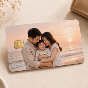 May include: A personalized credit card featuring a family portrait at the beach during sunset. The card has a gold-colored chip and is surrounded by a neutral-toned background with a wallet and decorative flowers.