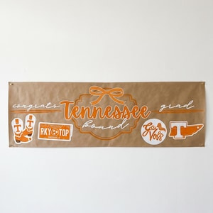 May include: A brown banner with orange text and graphics. The banner says "congrats Tennessee bound grad" with a bow graphic. Additional graphics include cowboy boots, a "RKY TOP Knoxville" sticker, a "Go Vols" circle, and a "T" graphic.