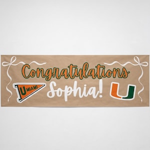 May include: A brown banner with the words "Congratulations Sophia!" in white and orange script. The banner includes the University of Miami logo and decorative white ribbons.