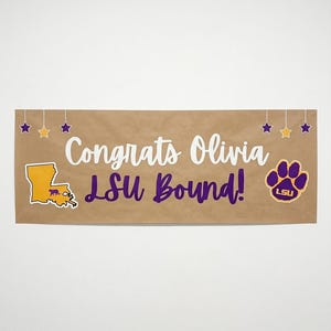 May include: A brown banner with the text "Congrats Olivia LSU Bound!" in white and purple. The banner includes a purple and gold Louisiana state outline, star accents, and a purple paw print with "LSU" inside.