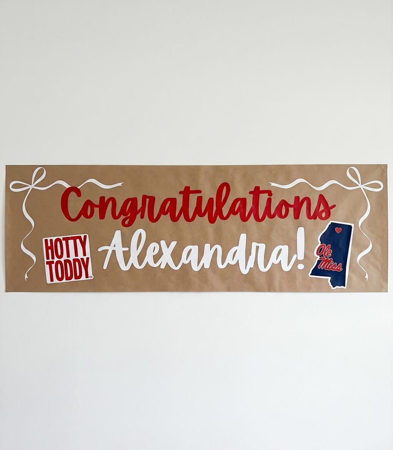 May include: A brown banner with the words "Congratulations Alexandra!" in red and white script. The banner includes a "Hotty Toddy" logo and a Mississippi state outline with "Ole Miss" text.