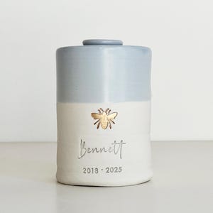 May include: A white ceramic mug with a black handle and the text "But First, Coffee" in a black, bold font. The mug is sitting on a white surface. The mug is approximately 4 inches tall.