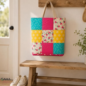 Peut inclure: Un sac fourre-tout matelassé composé d'un motif patchwork de neuf carrés. Le design présente du tissu rose vif à pois blancs, du tissu jaune à marguerites blanches et du tissu clair à motifs de fraises rouges et de feuilles vertes.
