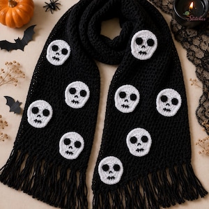 Puede incluir: Una bufanda negra de ganchillo con múltiples apliques de calaveras blancas con ojos, narices y bocas bordados en negro. La bufanda tiene un patrón de punto texturizado y largos flecos negros en ambos extremos. La palabra Stitches es visible.