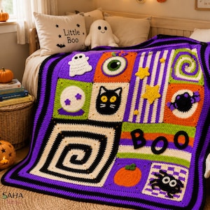 Op de afbeelding: Een handgemaakte gehaakte deken met een patchworkontwerp met Halloween-motieven, waaronder een witte geest, een groen oog, een zwarte kat, een spin, een pompoen en gele sterren. De deken heeft een paarse en zwarte rand en het woord BOO.