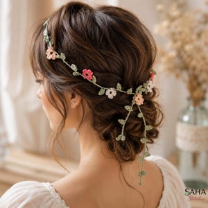 Könnte beinhalten: Ein handgefertigtes gehäkeltes Blumen-Haarband mit rosa, weißen und pfirsichfarbenen Blüten und grünen Blättern. Das Haarband wird im Haar getragen, mit einer Kaskade aus Blumen und Blättern. Das Bild zeigt den Hinterkopf einer Person, mit dem Text "SAHA Stitches".