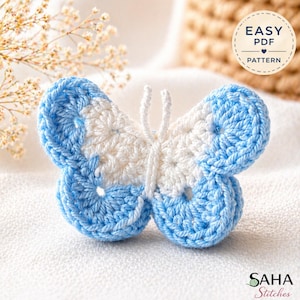 Pode incluir: Uma borboleta de crochê em tons de azul e branco, com antenas delicadas. As asas são uma combinação de fio azul claro e branco, criando um efeito texturizado. A imagem inclui o texto "EASY PDF PATTERN" e a marca "SAHA Stitches".