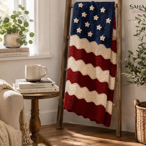 Könnte beinhalten: Eine gehäkelte Decke mit einem wellenförmigen amerikanischen Flaggenmuster, einem dunkelblauen Feld mit weißen Sternapplikationen und abwechselnden horizontalen Streifen in Creme und Dunkelrot, drapiert über einem hölzernen Leiterregal.