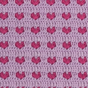 May include: A crocheted fabric featuring a repeating pattern of small, vibrant magenta hearts set against a soft, light lavender background. The texture is created with consistent, dense yarn stitches, forming a uniform grid of heart shapes throughout.