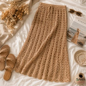 Puede incluir: Falda de crochet beige con cintura con cordón. La falda tiene un diseño de tejido abierto y un dobladillo festoneado. La imagen también incluye sandalias, gafas de sol y una revista.
