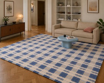 May include: A large rectangular area rug with a blue and off-white plaid pattern. The rug is placed on a hardwood floor in a living room setting. The rug's design features a grid of blue squares and lines against an off-white background.