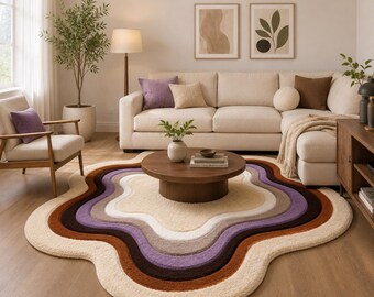 May include: A living room scene featuring a cream-colored sectional sofa, a wooden coffee table, and a unique, wavy-edged rug. The rug has layers of cream, purple, brown, and beige. Decorative pillows and framed art complete the cozy, inviting space.